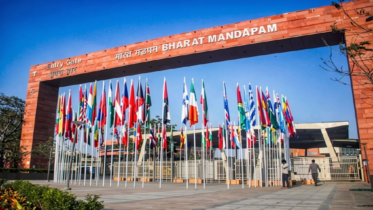 The Bharat Mandapam entry gate, signed in Hindi and English, with rows of national flags lining the approach.